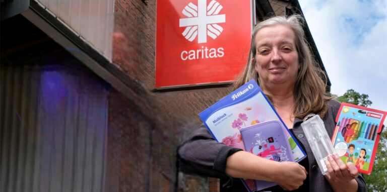 Eine Frau hält Malblock, Etui, Zirkel und Buntstifte in der Hand.