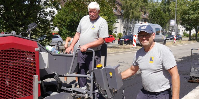 Zwei Bauarbeiter asphaltieren Woche die Rappaportstraße.