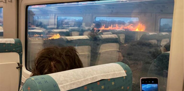 Fahrgäste fotografieren während einer Zugfahrt einen Waldbrand.