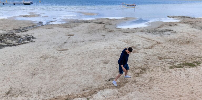 Ein Mann markiert die normale Wasserlinie am Strand.