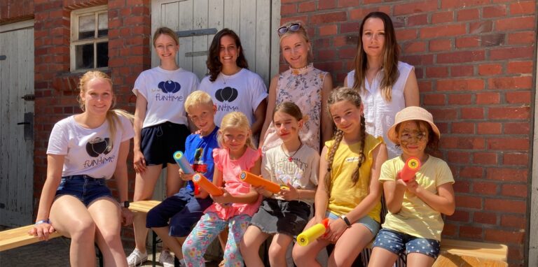 Frauen und Kinder sitzen am Prosper-Gutshof in Recklinghausen auf Holzbänken in der Sonne.