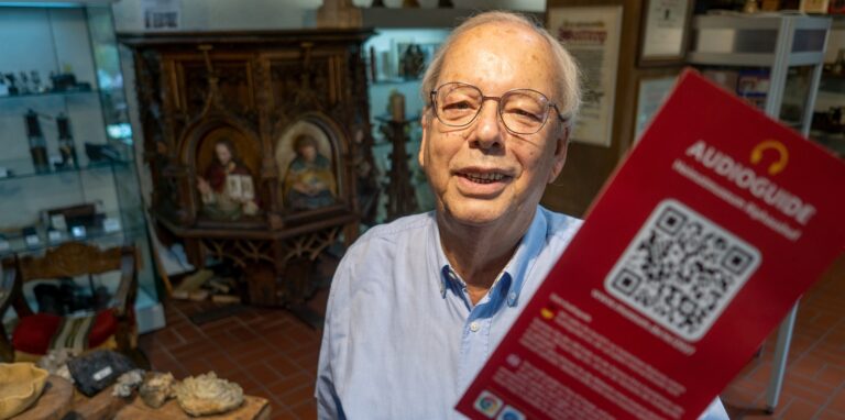 Ein Mann in einem Museum mit einem Flyer für einen Audioguide in der Hand.