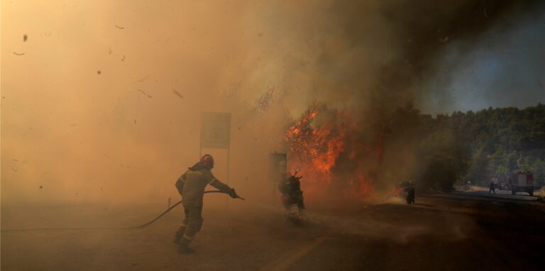 Ein Feuerwehrmann versucht, die Flammen neben Motorrädern auf einer Straße während eines Waldbrandes zu löschen.