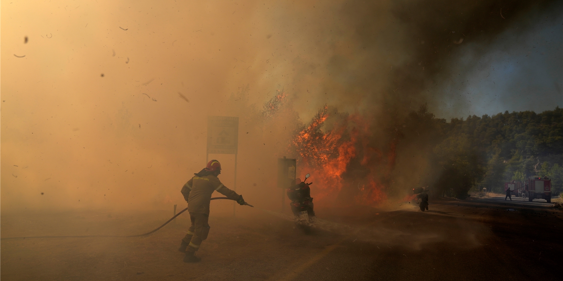 Ein Feuerwehrmann versucht, die Flammen neben Motorrädern auf einer Straße während eines Waldbrandes zu löschen.