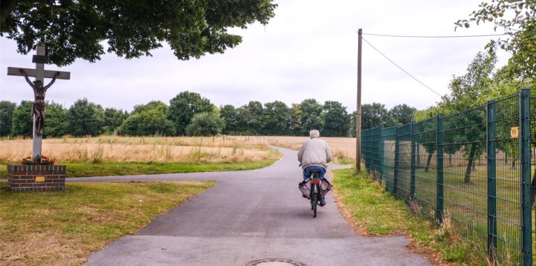 Ein Radler ist von hinten auf der Annastraße in Recklinghausen zu erkennen, links steht ein Wegekreuz, rechts ein Zaun