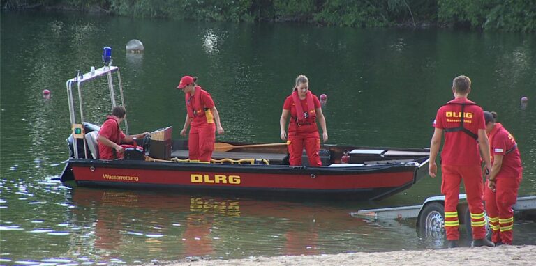 Mitarbeiter der DLRG suchen auf einem Badesee nach einem Jugendlichen.