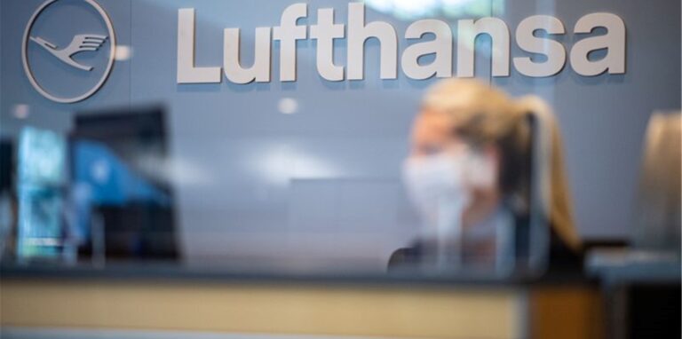 Eine Mitarbeiterin der Lufthansa sitzt mit ihrer Mund- und Nasenschutzmaske am Check-in im Flughafen Münster-Osnabrück.