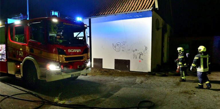 Ein Feuerwehrauto steht vor einem Haus. Feuerwehrleute gehen um das Haus herum.