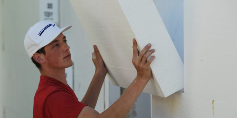 Ein Arbeiter montiert eine Styroporplatte zur Wärmedämmung an eine Fassade