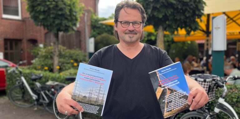 Dieter Mende steht mit zwei seiner Bücher in der Hand vor einer Hecke.