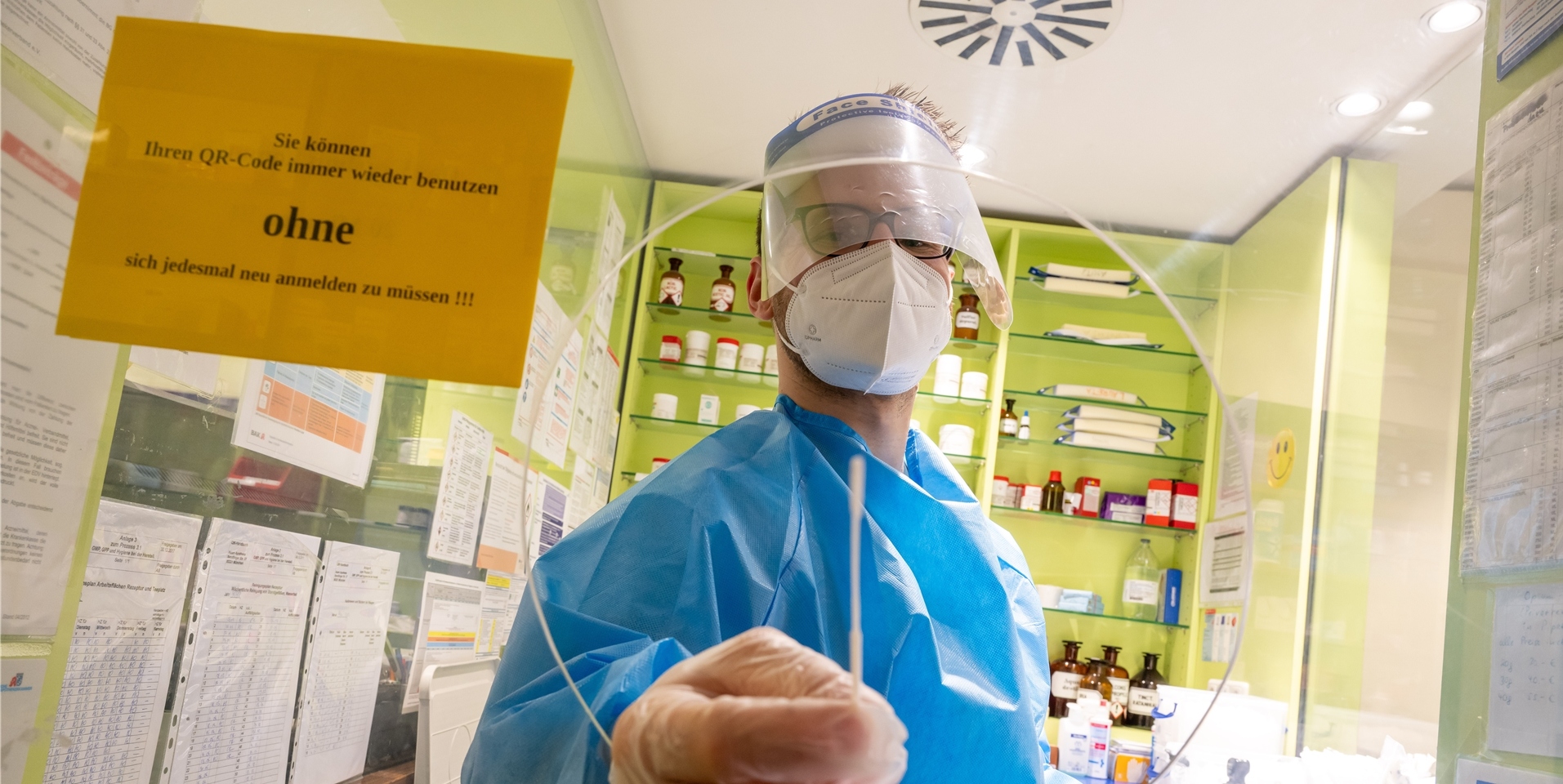 Ein Mitarbeiter einer Apotheke hält ein Teststäbchen für einen Corona-Schnelltest durch die Öffnung einer Scheibe. (Symbolfoto)