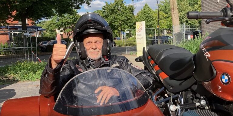 Eingerahmt von den Motorradfahrerinnen und -fahrern des Clubs Red Knights Dorsten sitzt Klaus Vogtländer im Beiwagen. Links steht Plegefachkraft und Bikerin Elke Siepmann, die die geniale Idee für diesen Ausflug hatte.