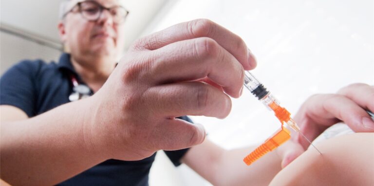 Ein Kinderarzt impft ein einjähriges Kind in den Oberschenkel mit dem Impfstoff Priorix (Lebendvirusimpfstoff gegen Masern, Mumps und Röteln).