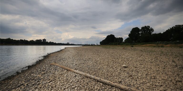 Wolken ziehen am Rhein über den bei niedrigem Pegelstand freigelegten Uferbereich.