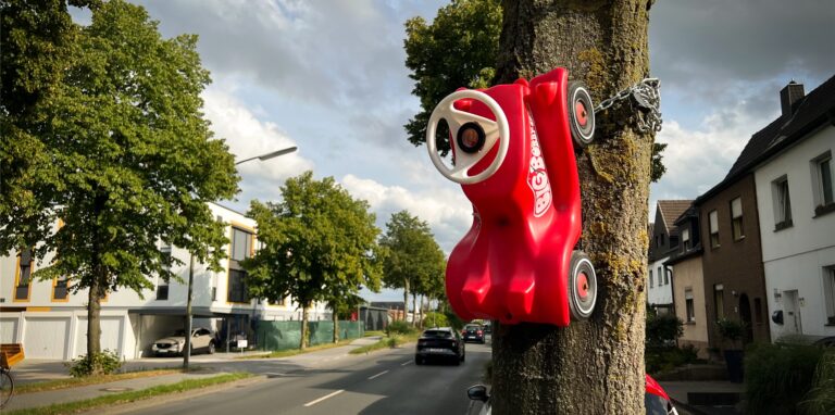 Eine stabile Kette hält das Bobby-Car an einem Baum, der an einer Dorstener Bundesstraße steht.