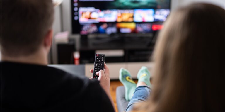 Ein Paar sitzt vor dem Fernseher, der Mann hält die Fernbedienung