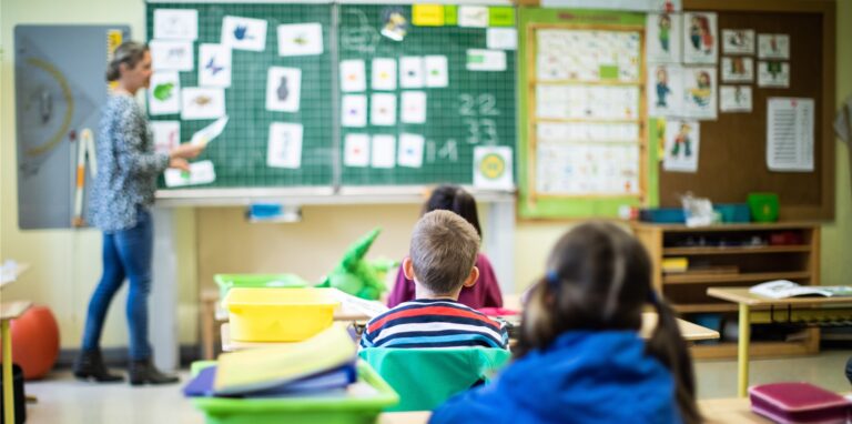 Schülerinnen und Schüler einer 1. Grundschulklasse sitzen mit Abstand in ihrem Klassenraum.