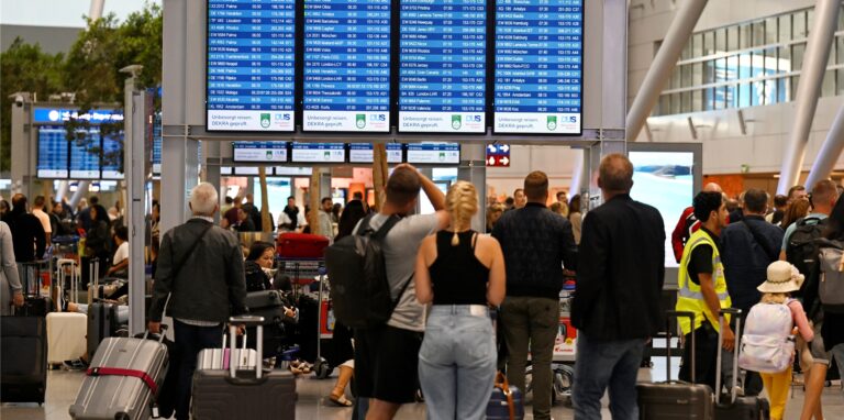 Passagiere stehen am Flughafen vor dem Flugplan.