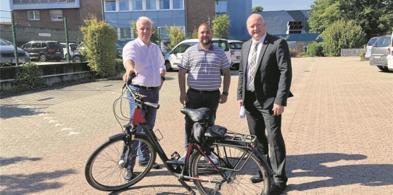 Marco Patruno und Sven Backhove vom Waltroper Kulturamt stehen mit Volksbank-Niederlassungsleiter Michael Scholten hinter einem Fahrrad auf dem Kundenparkplatz des Geldinstituts.