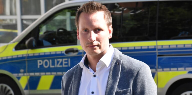 GdP-Vorsitzender Torsten Seiler steht vor einem Polizeiwagen.