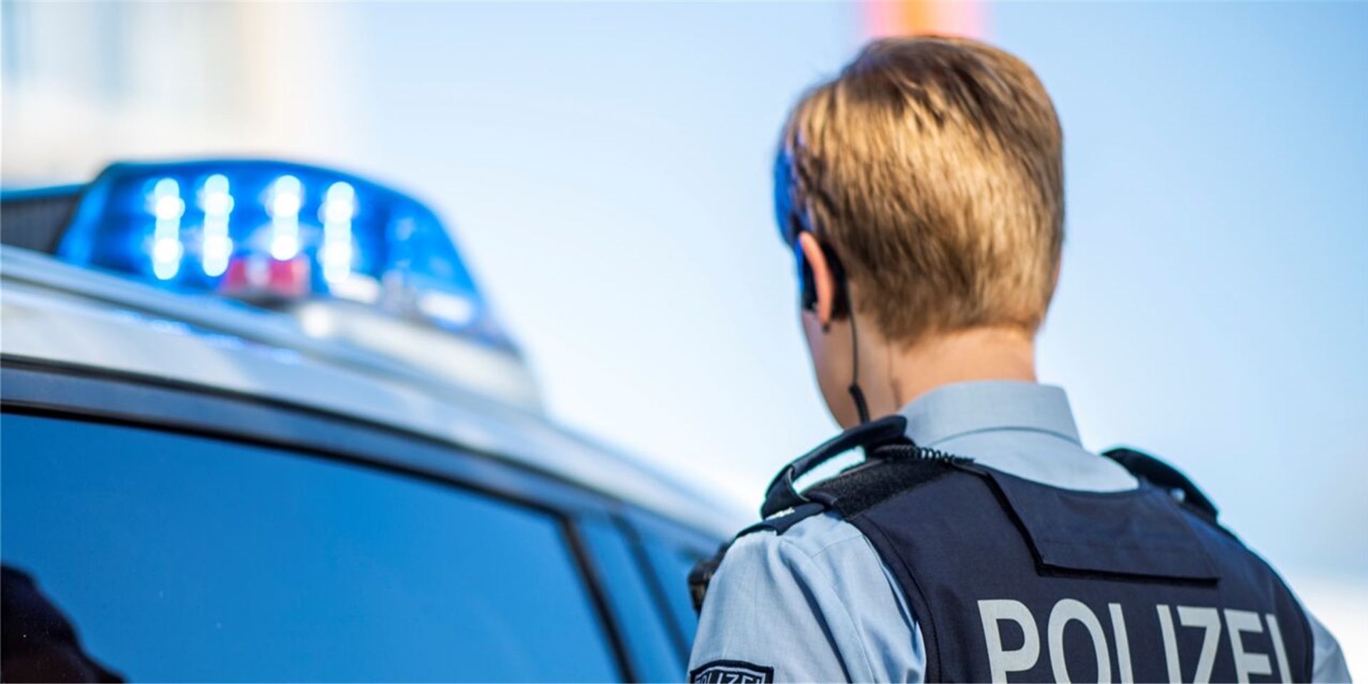 Ein Polizist steht mit Blick in Richtung seines Polizeiwagens. (Symbolbild)
