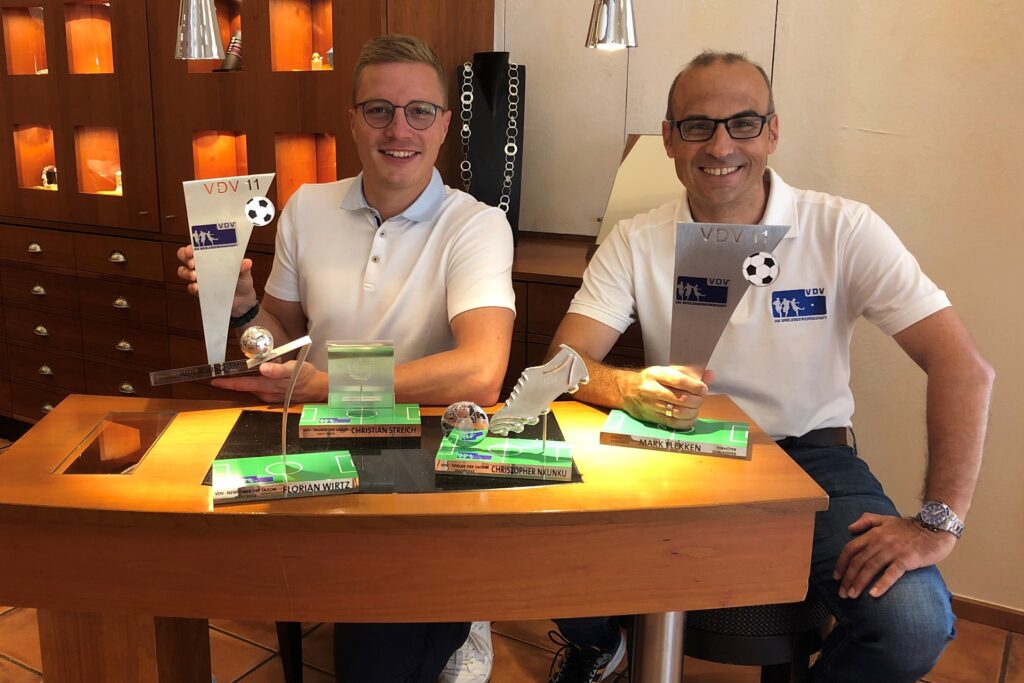 Max Zimmer (links) von Zimmer-Manufakturschmuck übergibt die Fußball-Trophäen an VDV-Geschäftsführer Ulf Baranowsky.