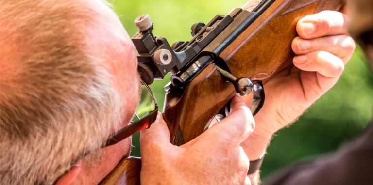 Ein Mann mit grauen Haaren zielt mit einem Gewehr.