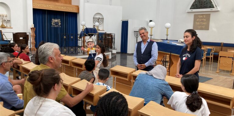 Isaac Tourgman von der Jüdischen Kultusgemeine in Recklinghausen steht vor syrischen Kindern und Erwachsenen in der Synagoge in Recklinghausen.