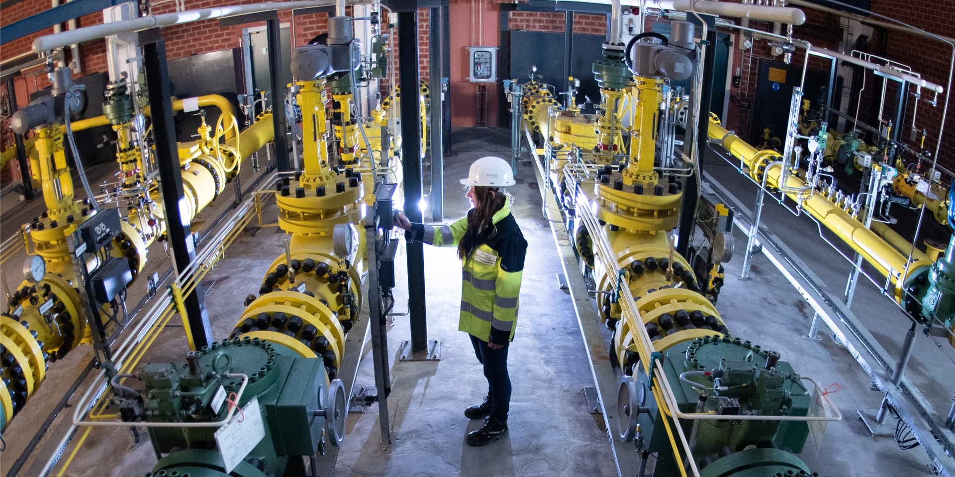 Eine Mitarbeiterin von Gasnetz Hamburg steht in der Gasübernahmestation Reitbrook zwischen verschiedenen Schienen zur Versorgung verschiedener Bereiche in Hamburg.