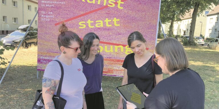 Museumsvolontärin Luise Klonowski (mit dem Rücken zur Kamera) erklärt an der Plakatwand gegenüber dem Museum, wie die App für die Ausstellung „Erweiterte Welten funktioniert.