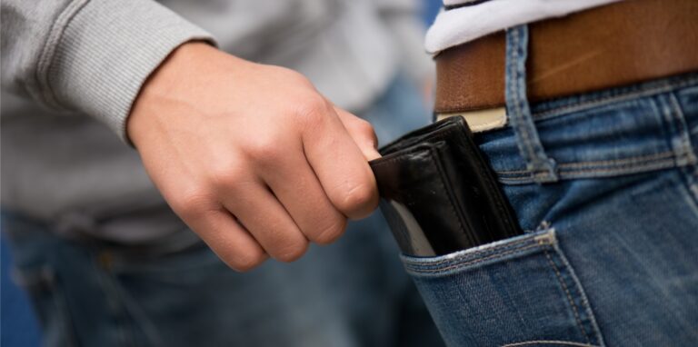 Eine Hand zieht eine Geldbörse aus der Gesäßtasche einer Jeanshose.