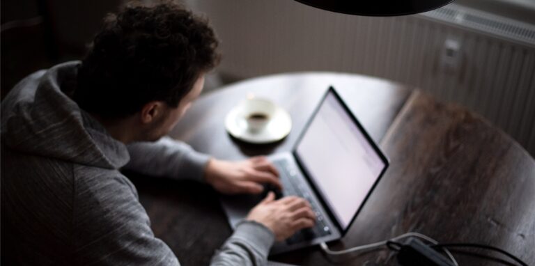Ein Mann sitzt im Homeoffice am Tisch an einem Laptop und arbeitet. (gestellte Szene).