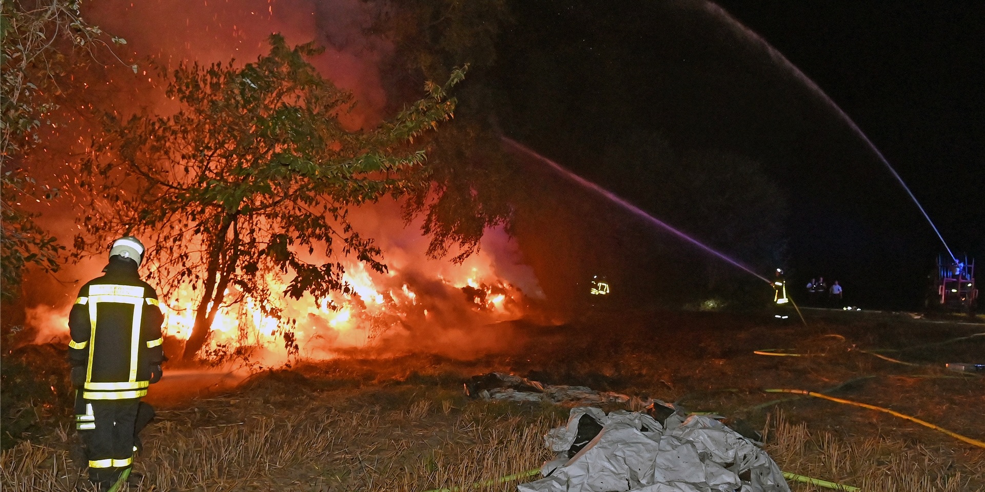 Ein Strohlager brennt in Lembeck. Feuerwehrleute löschen das Feuer.