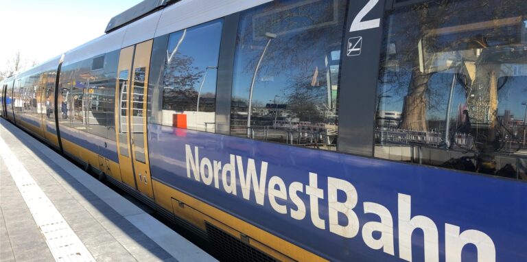 Ein Zug der NordWestBahn steht mit geschlossenen Türen in einem Bahnhof.