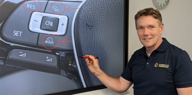 Martin Heidermann in Lembeck zeigt mit einem Kugelschreiber auf das Bild eines Bedienknopfes eines Fahrerassistenzsystems.