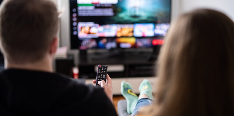 Ein Paar sitzt vor dem Fernseher, der Mann hält die Fernbedienung.