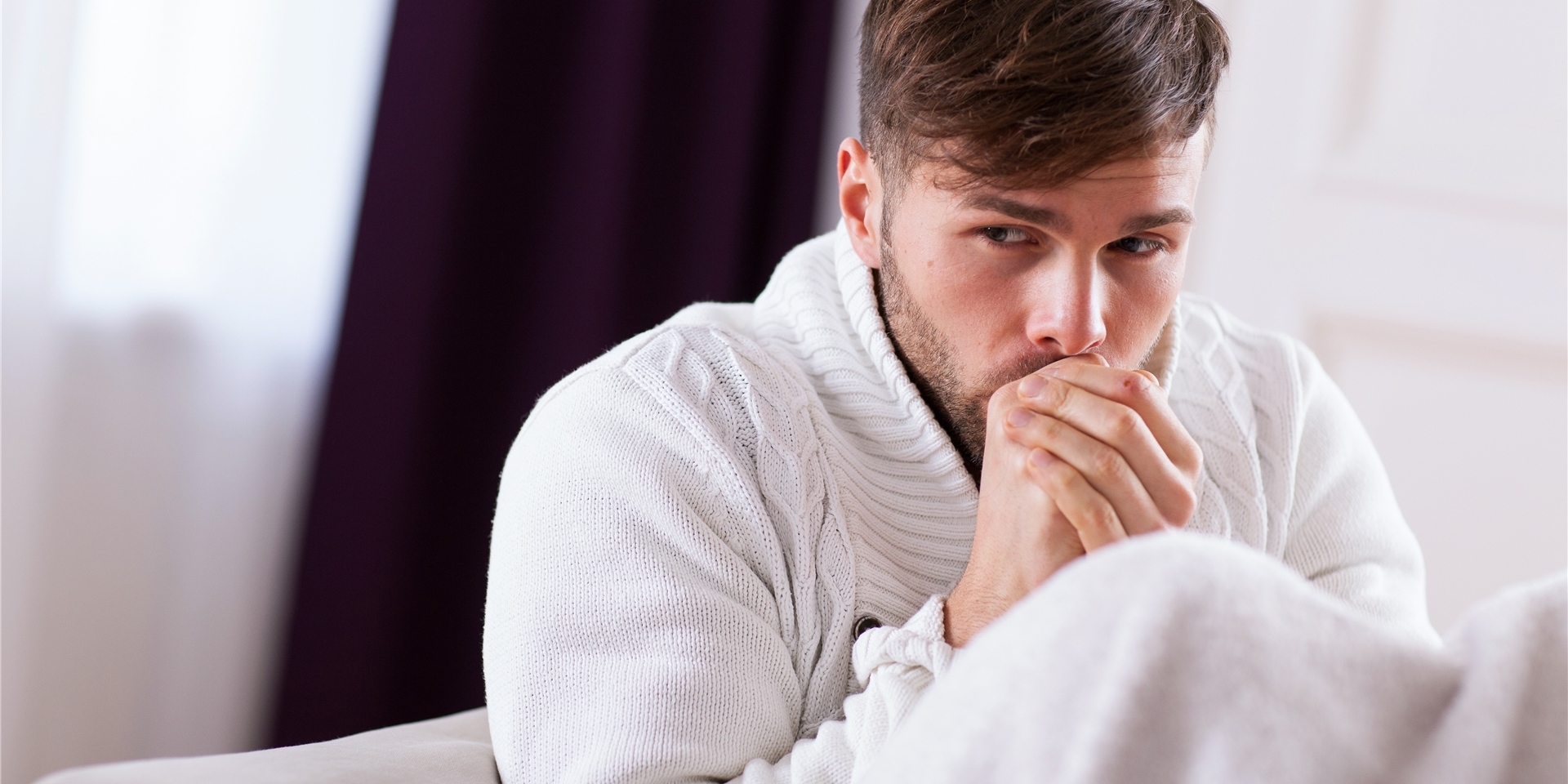 Ein Mann sitzt mit Decke auf der Couch und friert