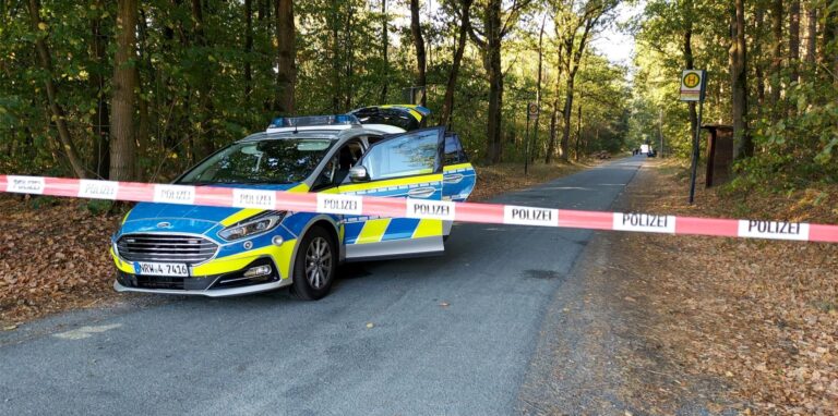 Ein Polizeiauto steht an einem mit Flatterband abgesperrten Waldweg in Greven (Kreis Steinfurt). Hier wurde die Leiche einer jungen Frau (25) im Gebüsch gefunden.