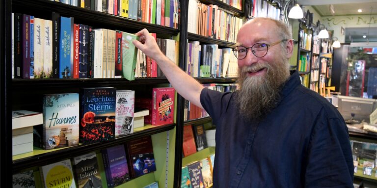 Buchhändler Wolfgang Tänzer steht in seinem Ladenlokal vor einem Regal und greift nach einem Buch.