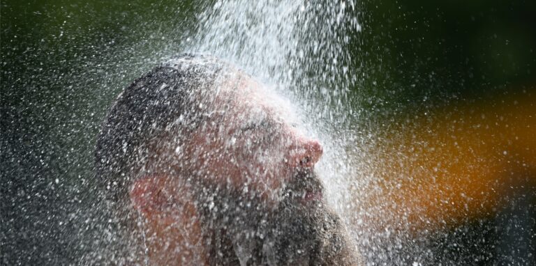 Ein Mann kühlt sich im Freibad unter einer Dusche ab.