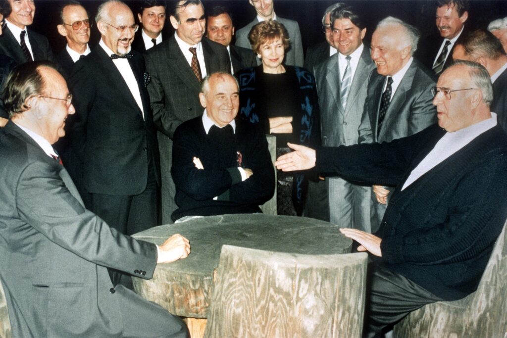 Bundeskanzler Helmut Kohl (r), der sowjetische Staatspräsident Michail Gorbatschow (M) und Bundesaußenminister Hans-Dietrich Genscher (l) unterhalten sich am 15.07.1990 in entspannter Atmosphäre an einem rustikalen Arbeitstisch in der freien russischen Natur. Bundeskanzler Helmut Kohl (r), der sowjetische Staatspräsident Michail Gorbatschow (M) und Bundesaußenminister Hans-Dietrich Genscher (l) unterhalten sich am 15.07.1990 in entspannter Atmosphäre an einem rustikalen Arbeitstisch in der freien russischen Natur.