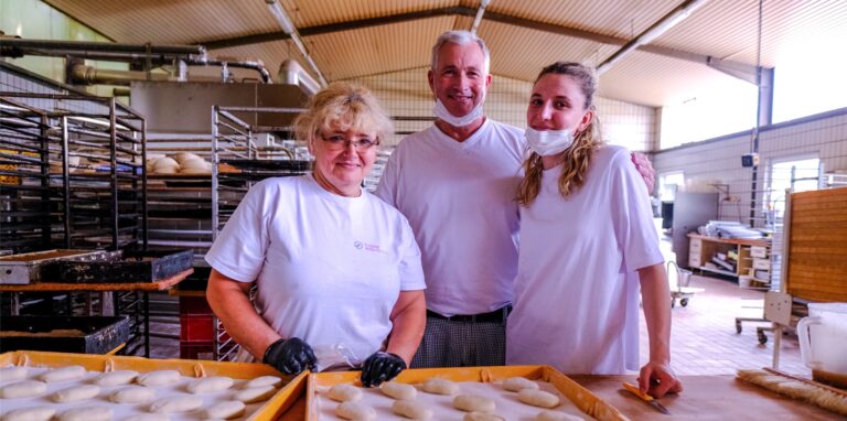 Zwei Frauen und ein Mann stehen in einer Backstube in Recklinghausen vor zwei Blechen mit Brötchen-Rohlingen.