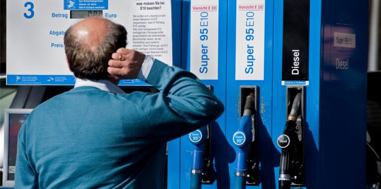 Ein Mann steht sichtlich verwirrt vor einer Super E10 Zapfsäule einer Tankstelle.