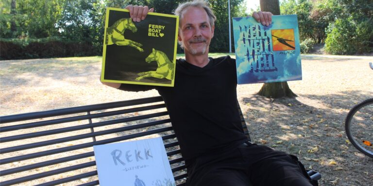 Ein Mann sitzt auf einer Bank und hält mehrere Schallplatten in die Höhe.