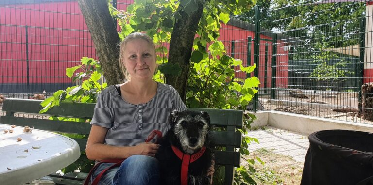 Marina Hinz sitzt auf einer grünen Holzbank und hält einen Hund an der Leine
