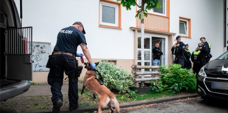 Ein Polizist mit Spürhund geht in das Wohnhaus des Tatverdächtigen in Essen.