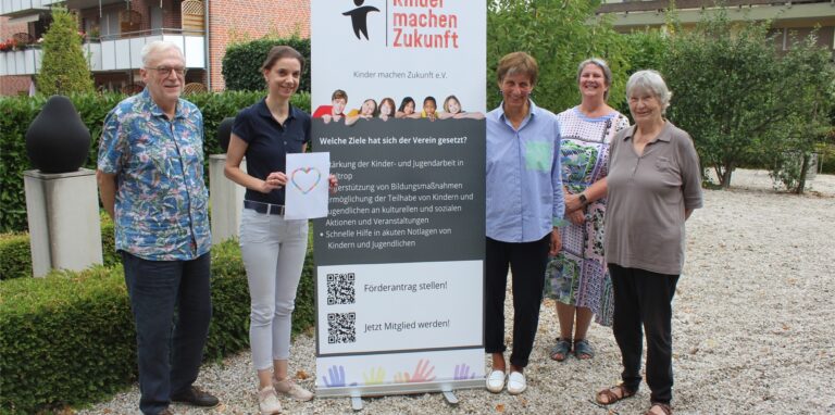 Fünf Personen sammeln sich um den Aufsteller von „Kinder machen Zukunft“.