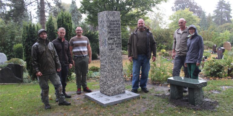Sechs Menschen stehen auf dem Friedhof Waltrop rund um eine Granit-Stele.