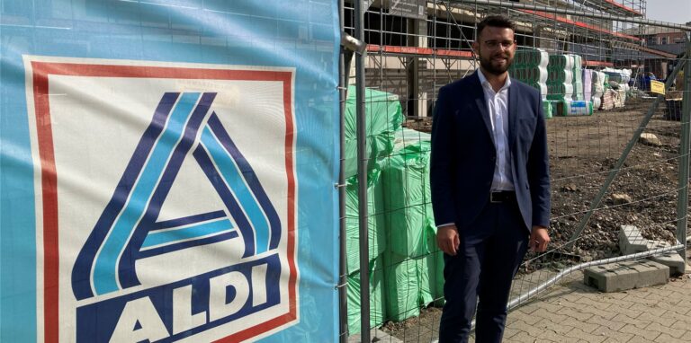 Ein Mann im Anzug steht neben einem Aldi-Banner an einem Bauzaun in Recklinghausen.