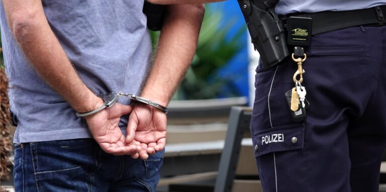 Ein Mann steht in Handschellen neben einem Polizisten.